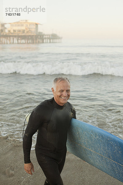 Ältere Surfer mit Brett am Strand