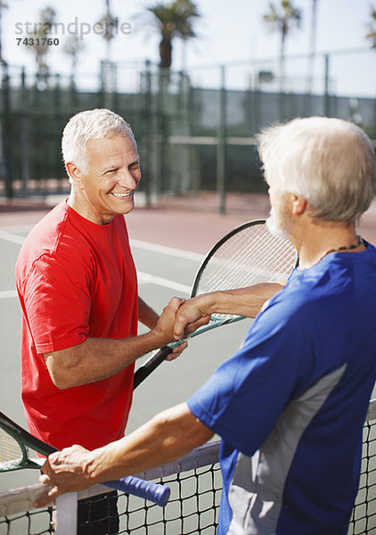 Ältere Männer beim Händeschütteln auf dem Tennisplatz
