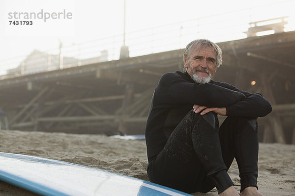 Älterer Surfer sitzend mit Brett am Strand