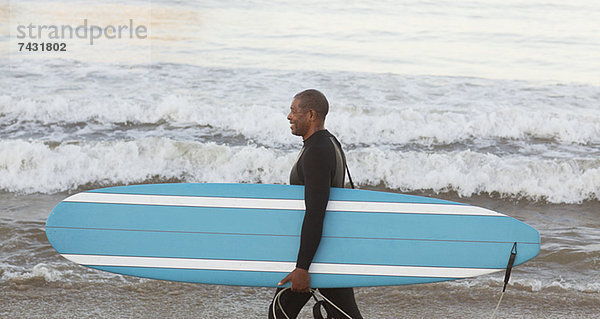 Ältere Surfer mit Brett am Strand