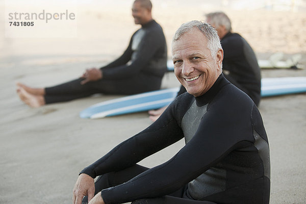 Ältere Surfer sitzen auf Brettern am Strand