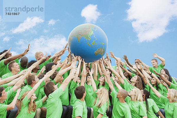 Team in grünen T-Shirts  die den Globus über Kopf heben.