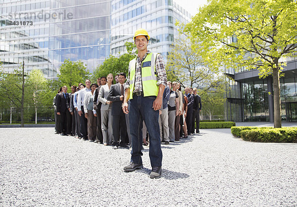 Porträt eines lächelnden Bauarbeiters mit Geschäftsleuten im Hintergrund