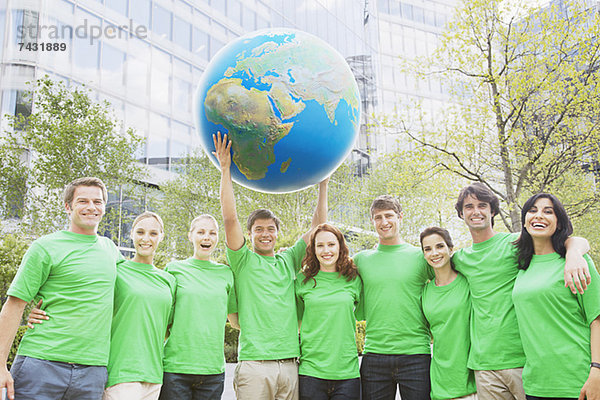 Porträt des Teams in grünen T-Shirts  die den Globus über Kopf heben.