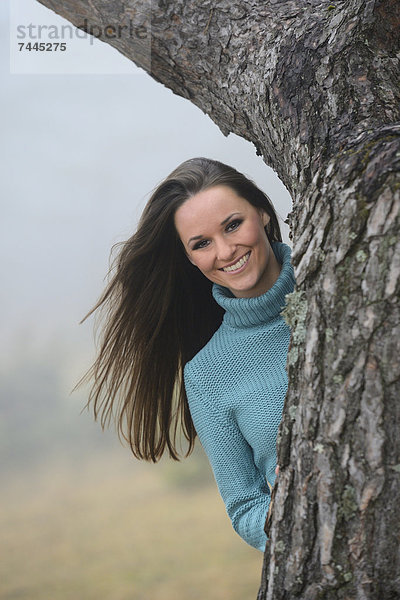 Brünette junge Frau an einem Baumstamm  Portrait
