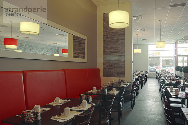 A restaurant interior  A long line of tables  and red banquette seating  Wooden chairs  Table place settings