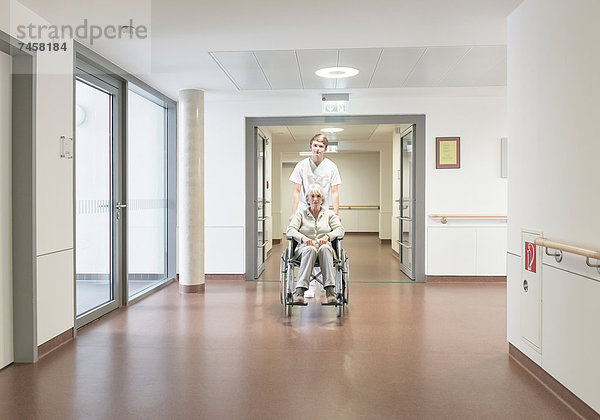 Krankenpfleger schiebt ältere Patientin im Rollstuhl