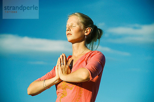 Frau meditiert unter blauem Himmel