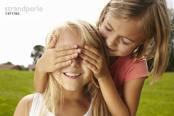 Lächelndes Mädchen bedeckt die Augen der Freunde