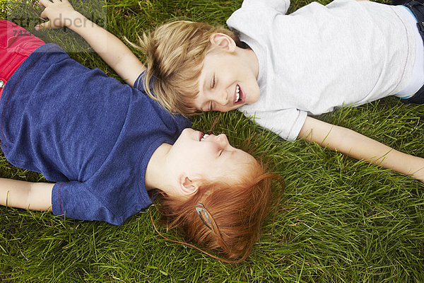 Lächelnde Kinder  die zusammen im Gras liegen.