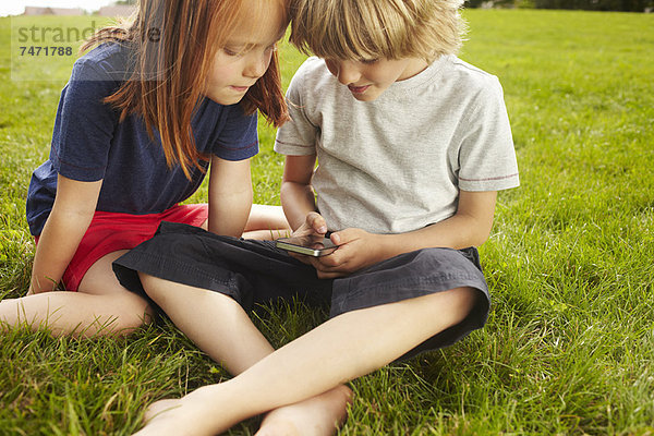 Kinder mit Handy im Gras