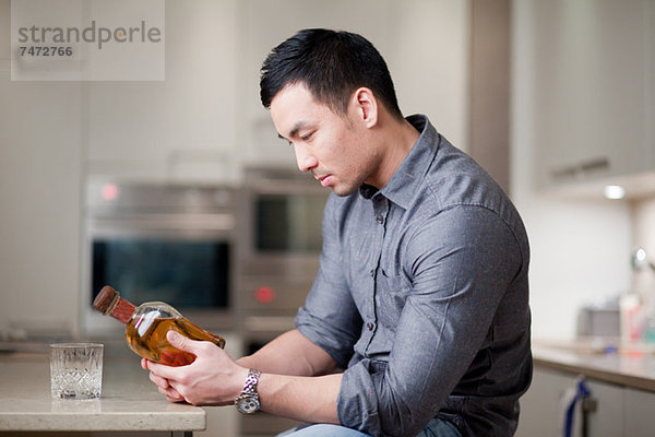 Mann untersucht Whiskeyflasche in der Küche