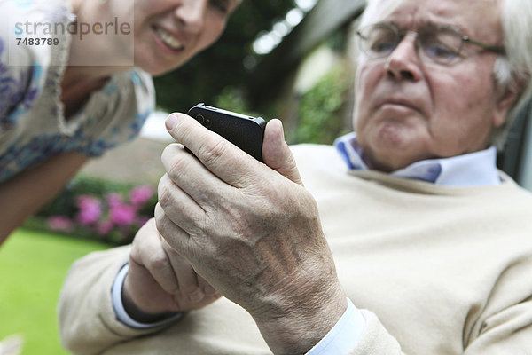 Junge Frau erklärt Senior die Bedienung eines Smartphones