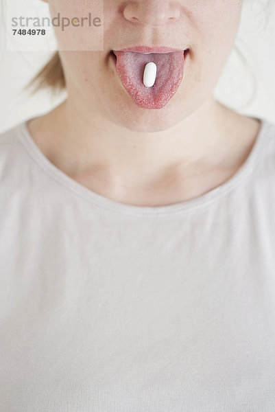 Frau mit einer weißen Pille oder Tablette auf der Zunge
