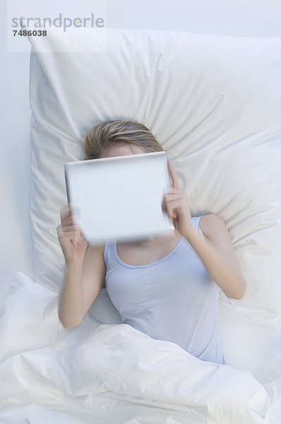 Deutschland  Junge Frau mit digitalem Tablett auf dem Bett liegend