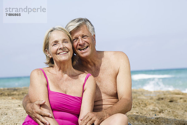 Spanien  Seniorenpaar auf Felsen am Strand sitzend  lächelnd