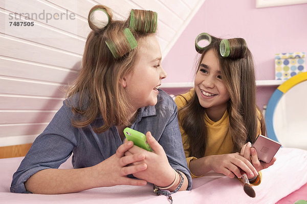 Mädchen mit Haarrollen liegend und beobachtend Smartphone  lächelnd