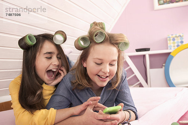 Mädchen mit Haarrollen liegend und beobachtend Smartphone  lächelnd