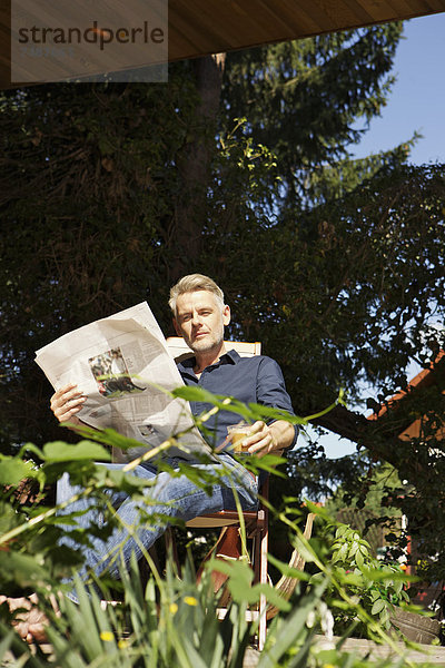 Erwachsener Mann auf der Terrasse sitzend und Zeitung lesend