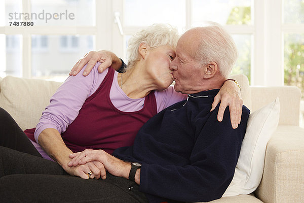 Deutschland  Düsseldorf  Seniorenpaar beim Küssen und Entspannen zu Hause