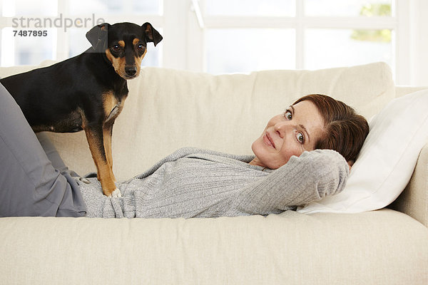 Reife Frau auf dem Sofa liegend mit Hund