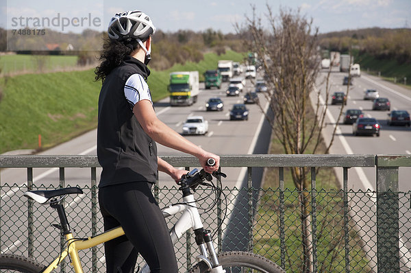 Deutschland  Mittlere erwachsene Frau mit Mountainbike auf Brücke mit Blick auf den Verkehr auf der Autobahn
