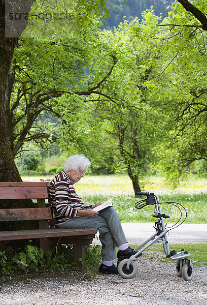 Österreich  Seniorin sitzend auf Bank und Lesebuch