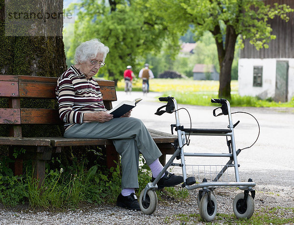 Österreich  Seniorin sitzend auf Bank und Lesebuch