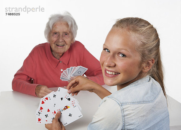 Seniorin und Teenagerin beim Kartenspielen  lächelnd