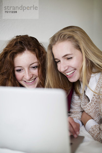 Glückliche junge weibliche Freunde  die ihren Laptop zusammen im Bett benutzen.
