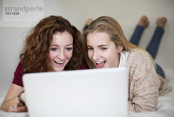 Überraschte junge Mädchen  die im Bett liegend den Laptop benutzen.