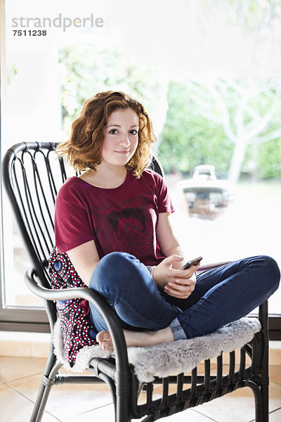 Porträt eines jungen Mädchens mit Handy  das sich zu Hause auf dem Sessel entspannt