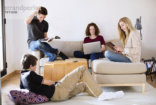 Junge Freunde mit Magazin  Laptop und digitalem Tablett im Wohnzimmer