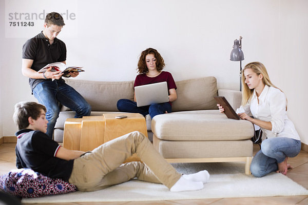 Junge Jungen und Mädchen mit Magazin  Laptop und digitalem Tablett im Wohnzimmer