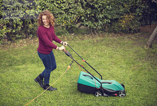 Fröhliches junges Mädchen schiebt elektrischen Rasenmäher auf Gras