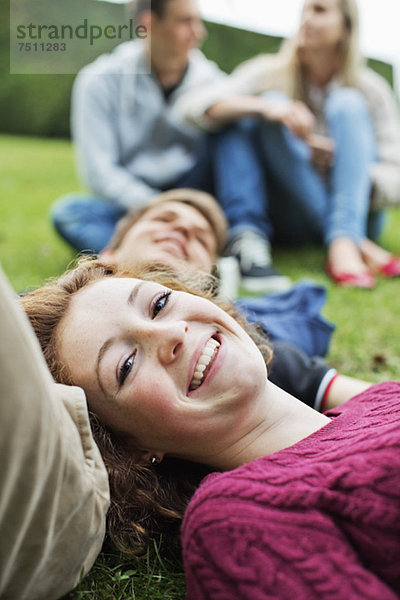 Porträt eines glücklichen jungen Mädchens mit Kopf auf dem Bauch des Jungen und einem Paar im Hintergrund im Park.