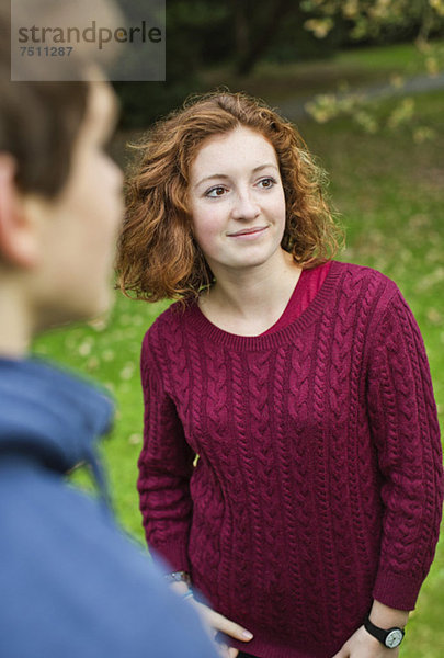 Junges Mädchen in kastanienbraunem Pullover mit Freund im Vordergrund im Park