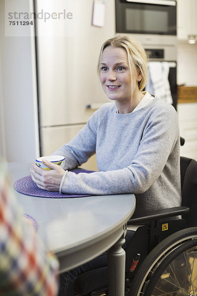 Behinderte mittlere erwachsene Frau im Rollstuhl  die einen Freund in der Küche ansieht.