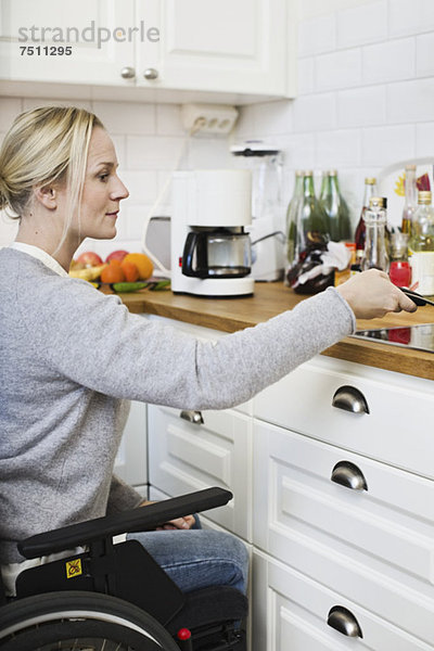 Behinderte mittlere erwachsene Frau im Rollstuhl in der Küche