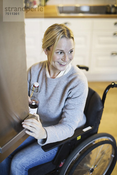 Fröhliche behinderte Frau mit der Flasche  die beim Schließen der Kühlschranktür in der Küche wegschaut.