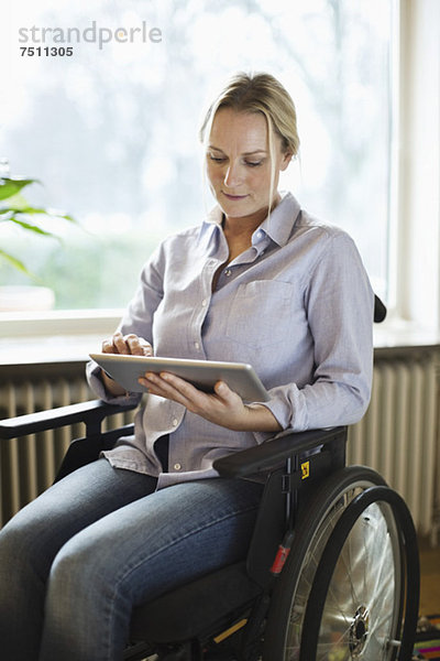 Behinderte Frau  die zu Hause im Rollstuhl sitzt und ein digitales Tablett benutzt