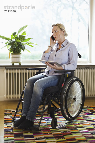 Behinderte Frau mit digitalem Tablett  die zu Hause im Rollstuhl sitzt.