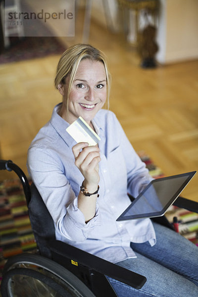 Portrait der glücklichen Frau im Rollstuhl mit digitalem Tablett mit Kreditkarte