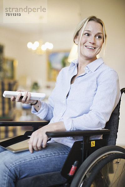 Fröhliche behinderte Frau im Rollstuhl mit digitalem Tablett und Fernbedienung