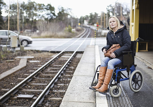 Behinderte Frau im Rollstuhl beim Warten auf den Zug am Bahnhof
