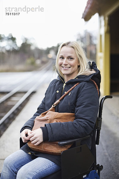 Porträt einer glücklichen behinderten Frau im Rollstuhl auf dem Bahnsteig des Bahnhofs