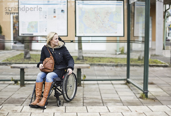 Behinderte Frau im Rollstuhl wartet an der Bushaltestelle