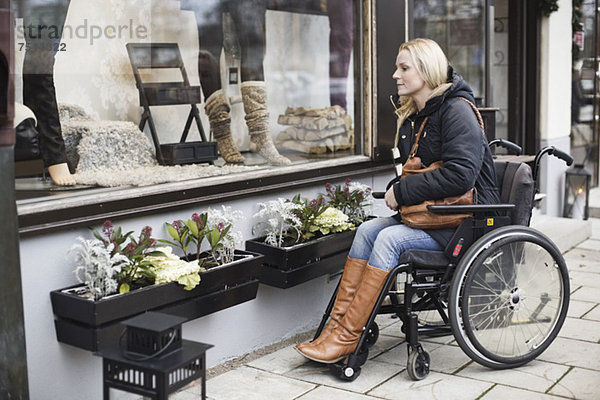 Behinderte Frau im Rollstuhl mit Blick ins Schaufenster