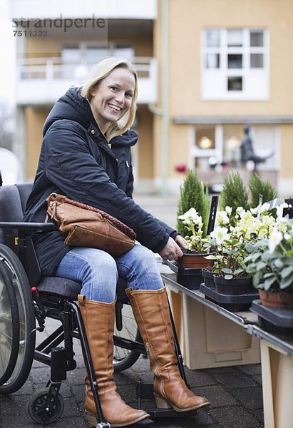 Porträt einer behinderten Frau im Rollstuhl bei der Pflanzenwahl in der Gärtnerei