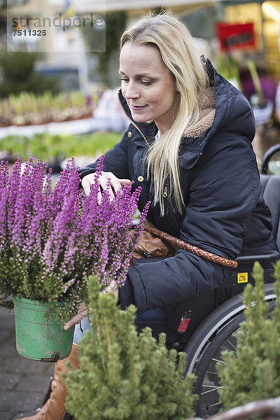 Behinderte Frau im Rollstuhl bei der Pflanzenwahl im Gartencenter